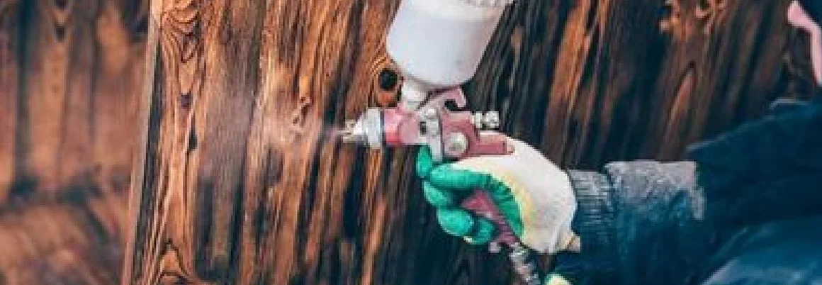 Person lackiert Holz mit Farbspritzpistole